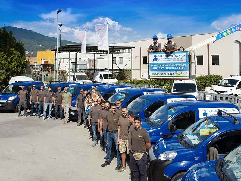 Il personale di S.R. Termotecnica in divisa accanto ai furgoni aziendali, davanti alla sede; due tecnici sul cestello della piattaforma aerea